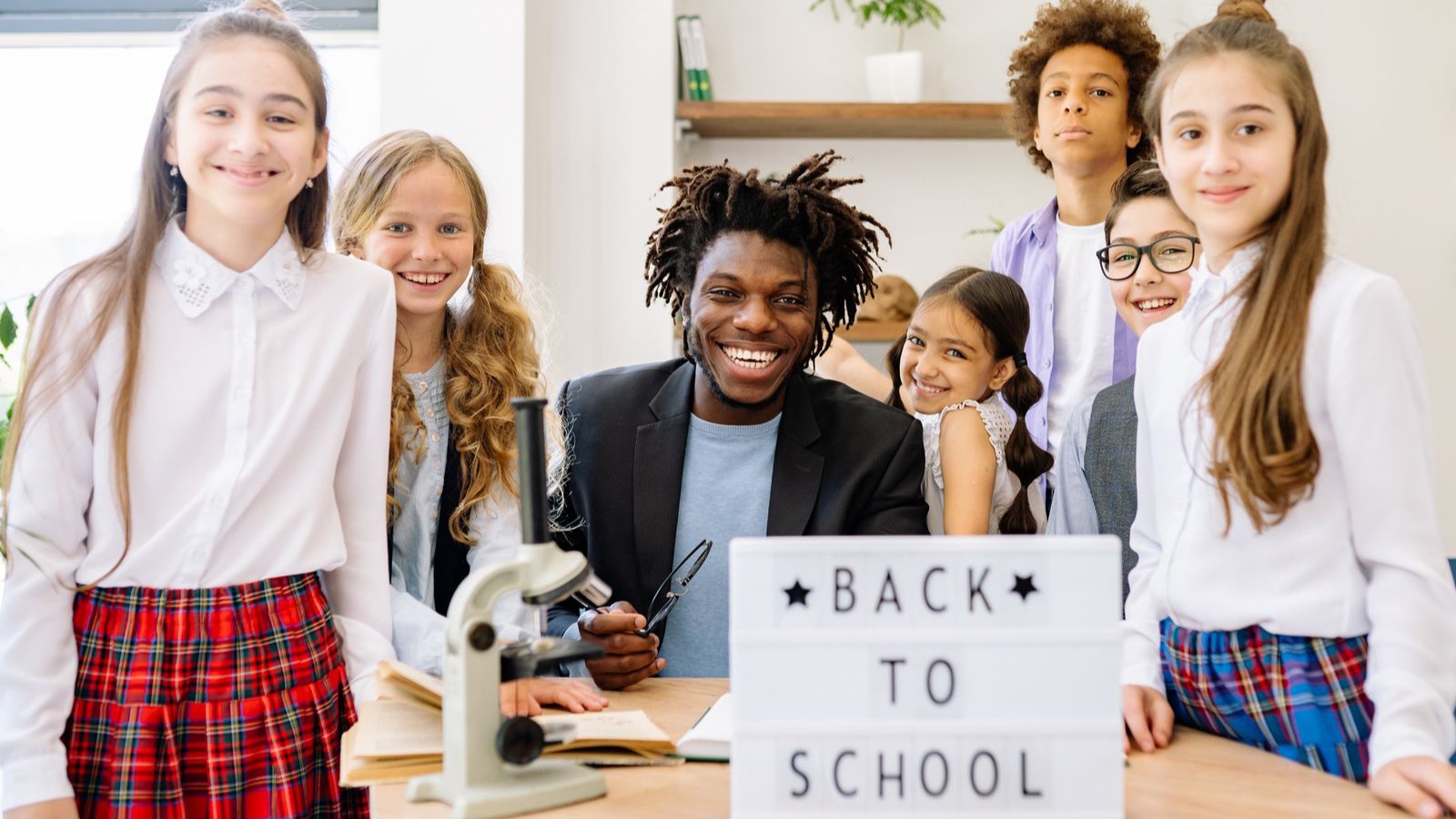 A teacher and a multi-ethnic group of students smiling together around a table in a classroom