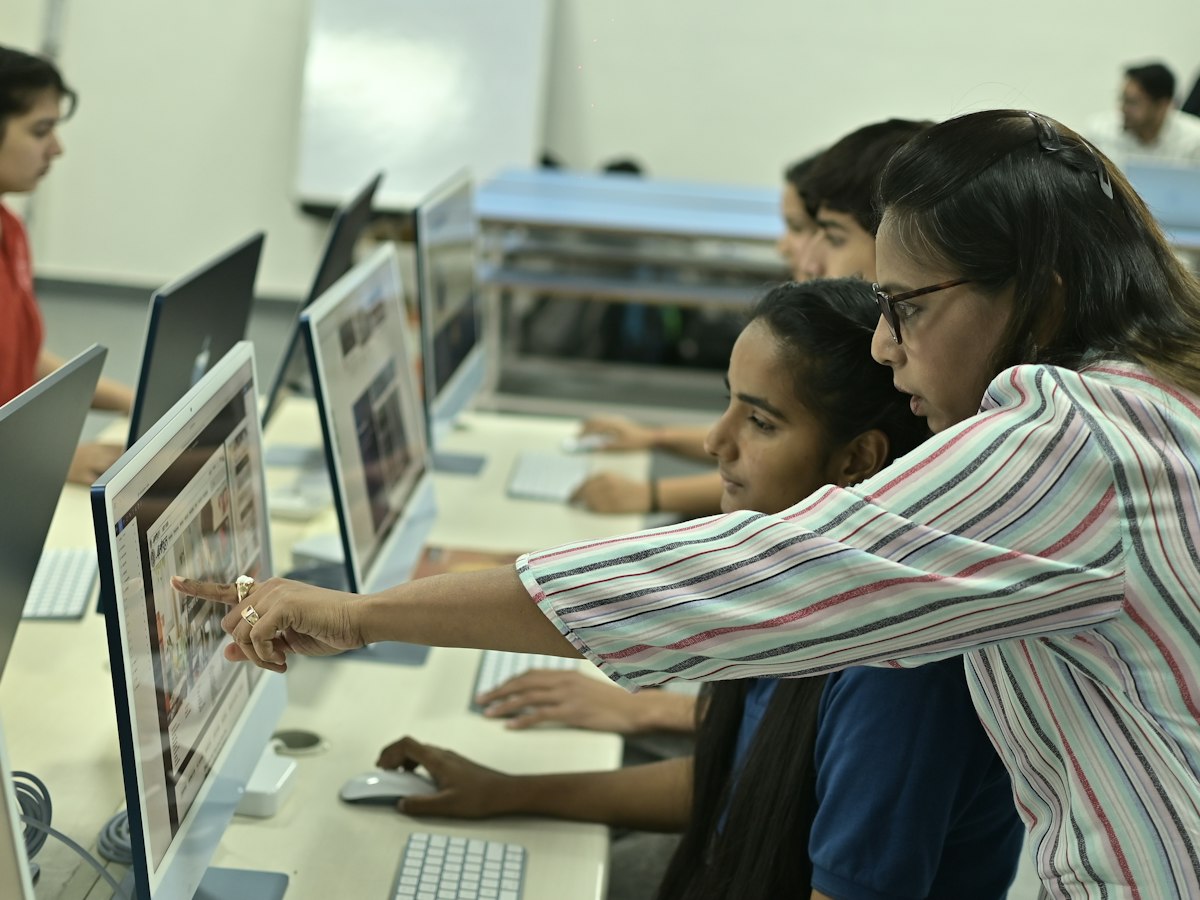 A teacher pointing at a student's screen in a computer lab