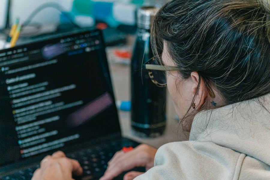 An adult typing at a laptop with code open on screen